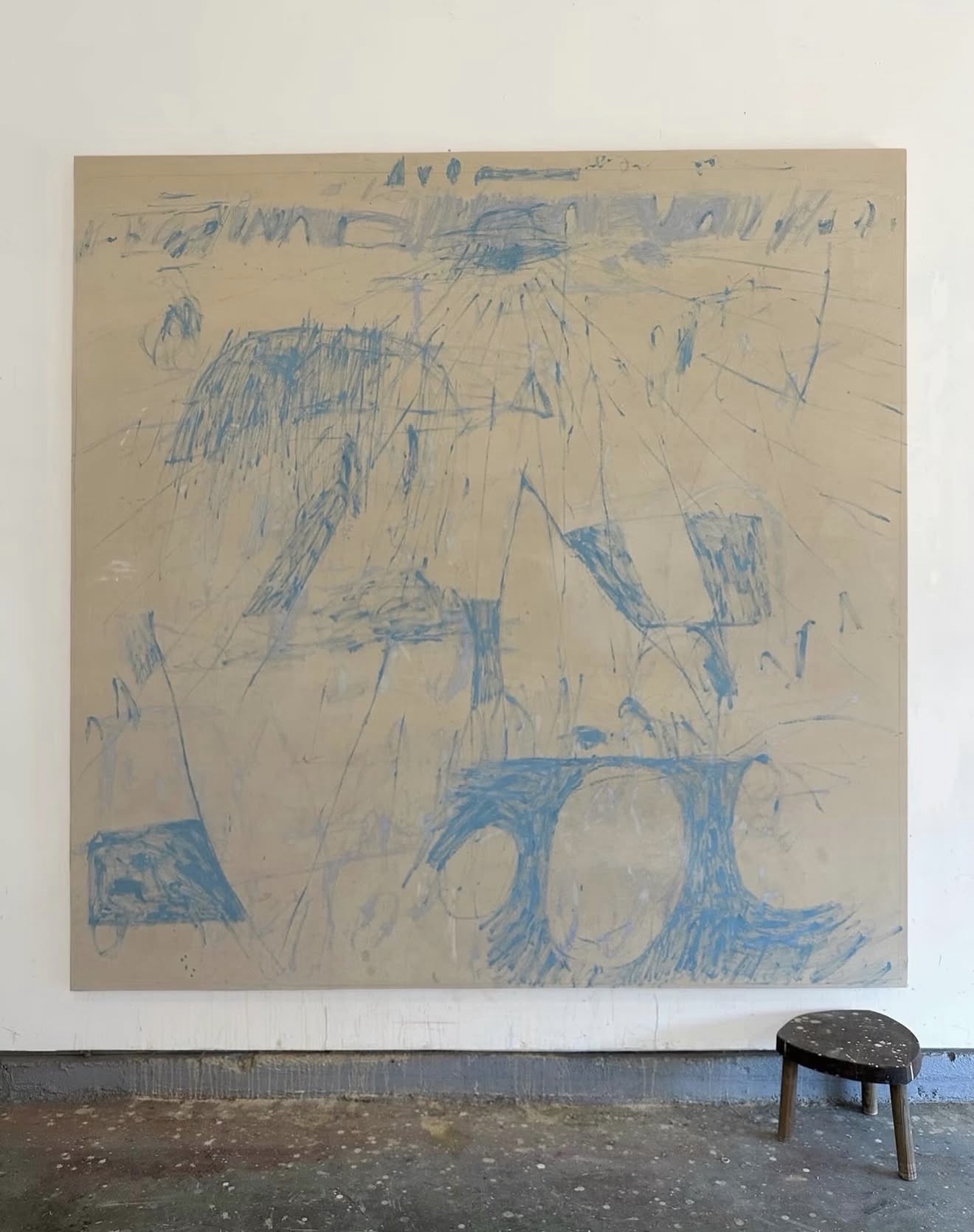 A large tan canvas with blue gestural drawings by Jonathan Todryk, leaning in the studio